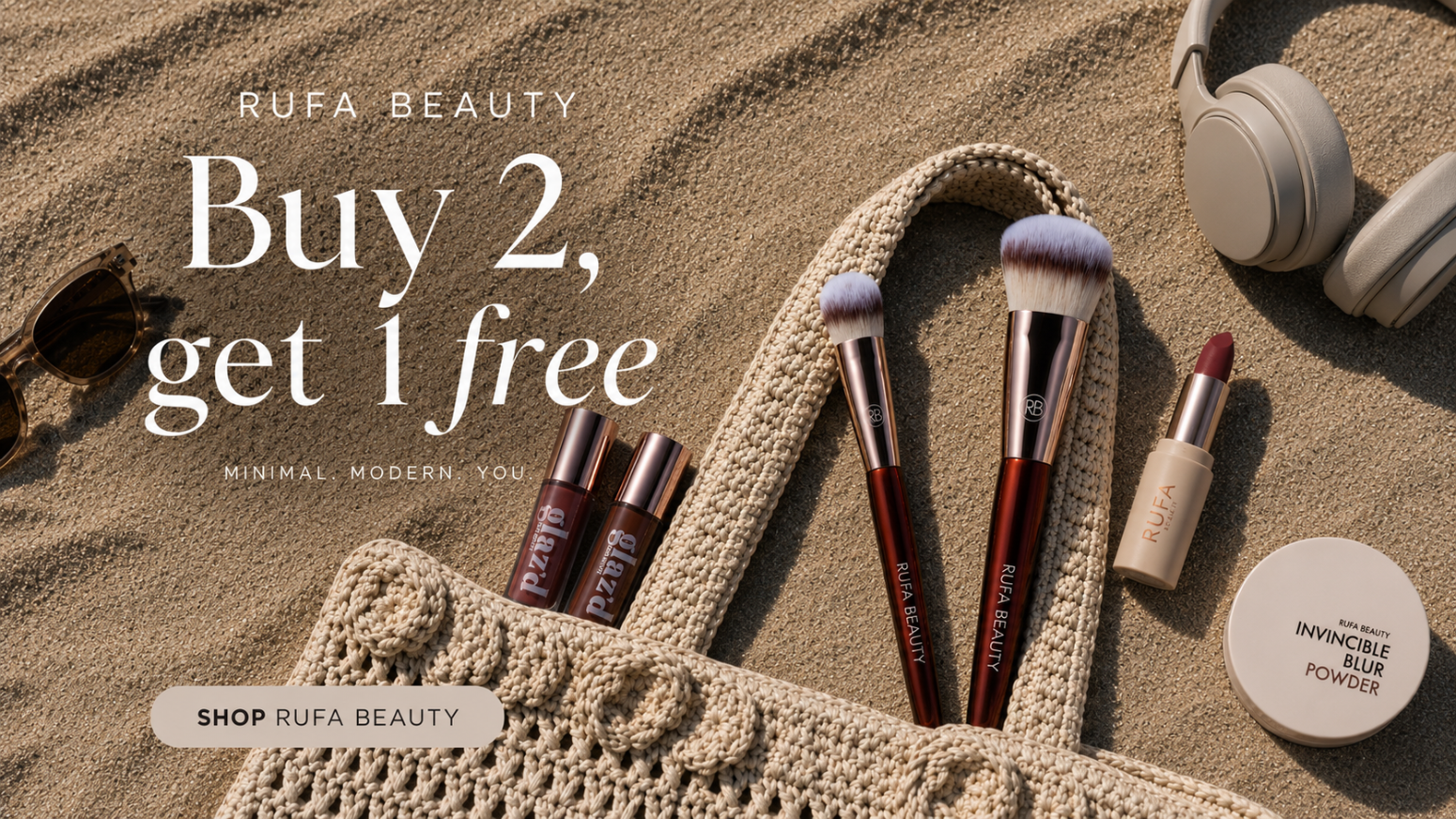 Rufa Beauty makeup products including brushes, lipsticks, and a compact on sand with promotional text.